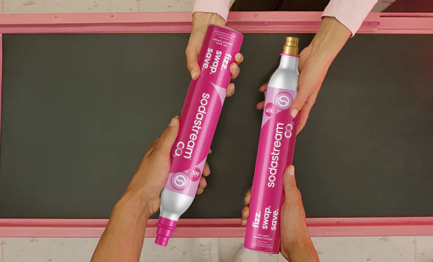 Two people exchanging pink Sodastream CO2 cylinders across a counter
