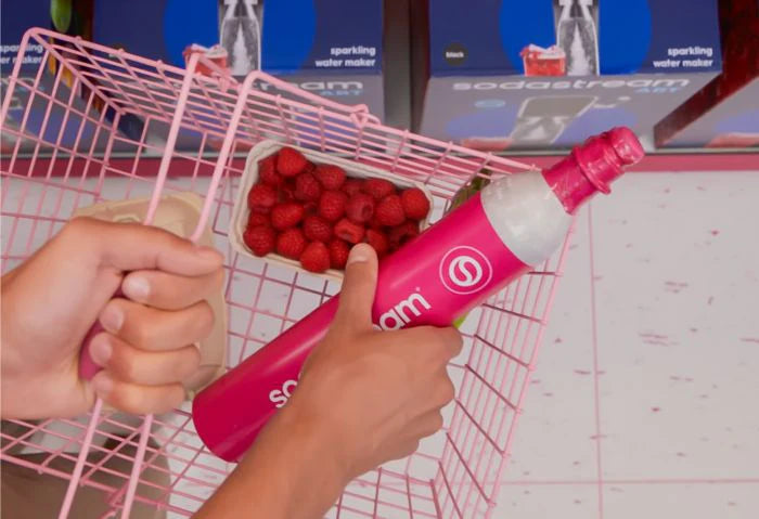 Person placing a pink Sodastream CO2 cylinder into a shopping basket