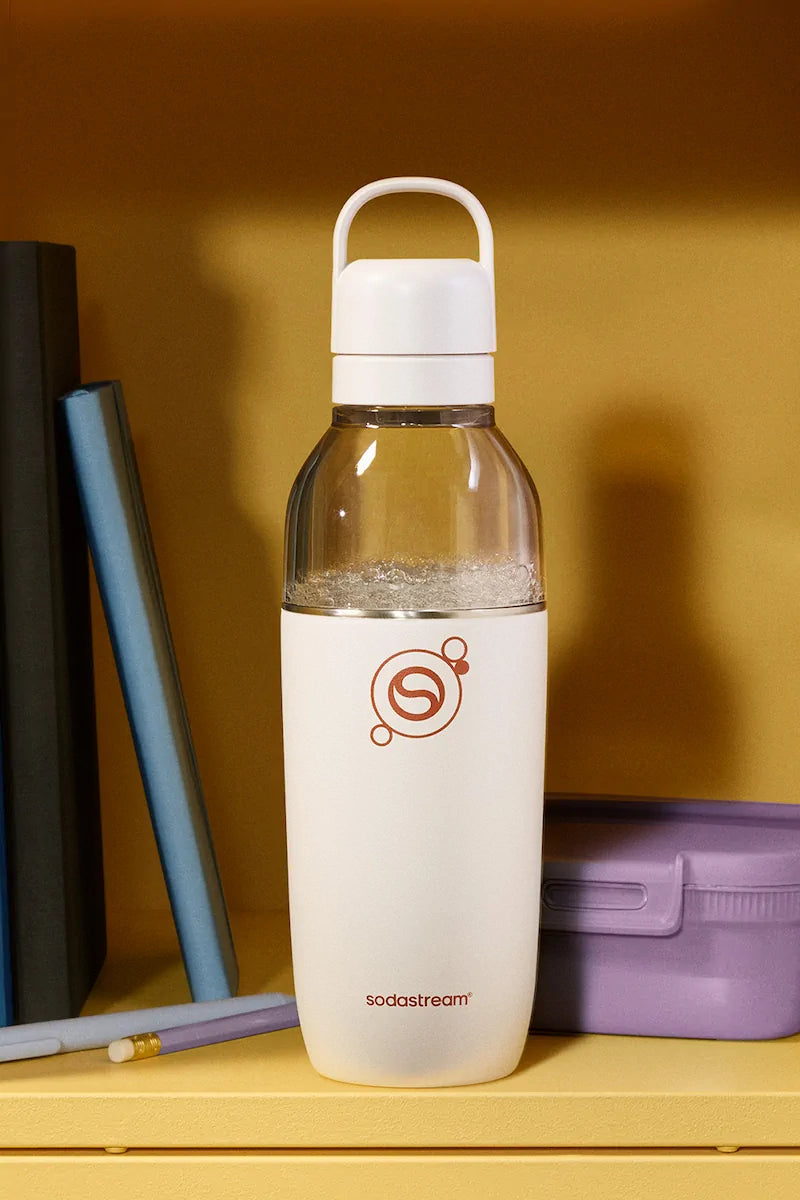 Sodastream Fizz & Go Easy Mix Sand bottle filled with sparkling water, on a shelf beside books and a lunch box