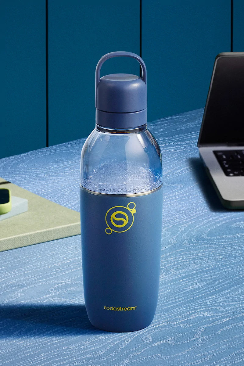 Sodastream Fizz & Go Easy Mix Storm (navy blue) bottle filled with sparkling water, on a blue desk beside a laptop