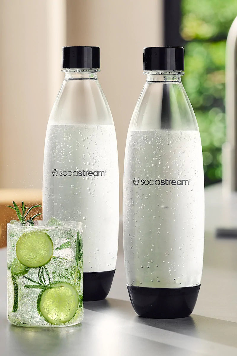 Two Sodastream 1 litre Fuse bottles of sparkling water next to a glass with ice and lime